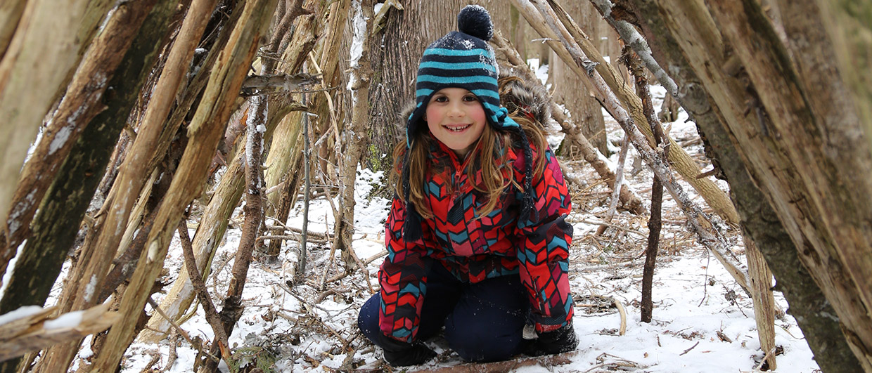 young girl sits inside forest shelter