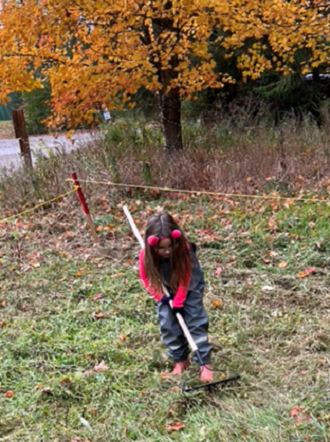 Nature School student using a rake to clear the overgrown sandbox at Kortright Centre